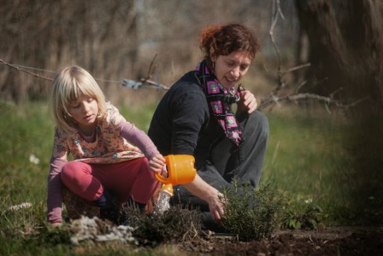 Frau und Kind sitzen gemeinsam im Gras. Das Kind spielt mit einer Spritzkanne.