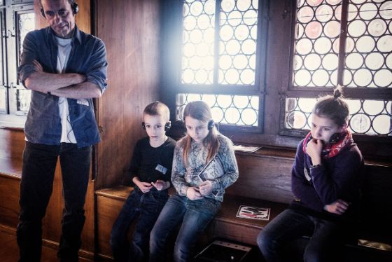 Mann mit drei Kindern im Museum. Sie sitzen und hören eine Audio.