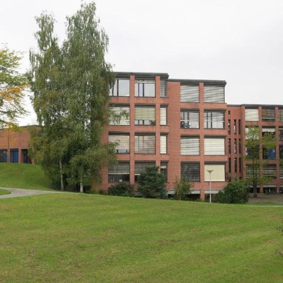 A view of the Röhrliberg school building facade with a meadow and trees in the foreground