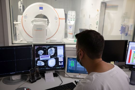 Radiologe sitzt vor dem Computer, im Hintergrund der Computertomograph