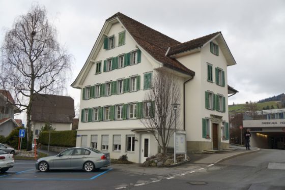 Seitenansicht mit Auto im Vordergrund, gelbe Fassade und braunem Dach.